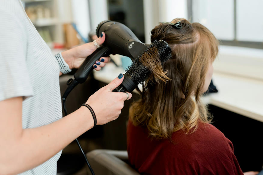 Une coiffeuse réalise un brushing à une femme assise dans un salon de coiffure