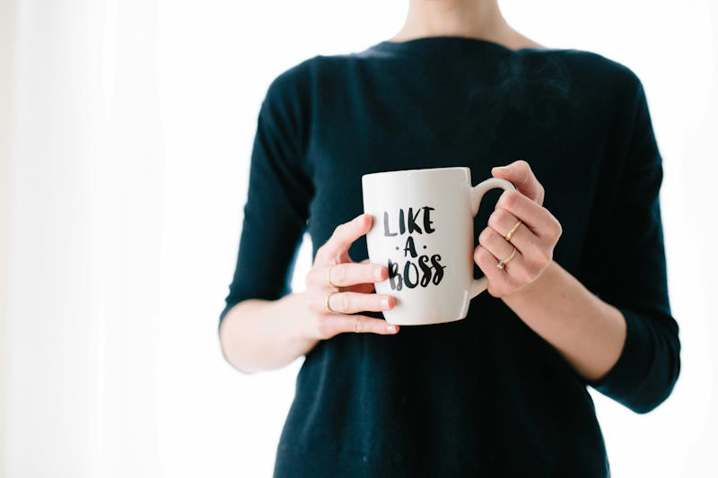 Une femme habillée élégamment et sobrement en noir, tient dans ses mains une tasse avec une inscription "like a boss".